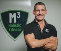 a man standing in front of a sign that says m3 holistic fitness