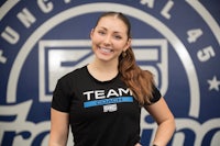a woman in a black t - shirt standing in front of a team logo