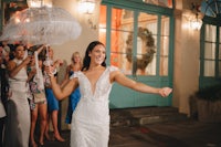 a bride in a white dress holding an umbrella in front of a crowd of people
